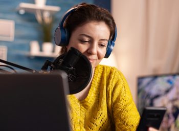 Blogger woman recording video for her blog in home studio reading messages on smartphone. On-air online production internet broadcast show host streaming live content for social media.